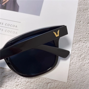 Close-up of sleek black sunglasses temple with signature gold V logo on textured base