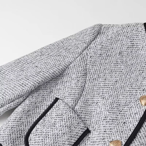 Detail of grey tweed jacket showing fabric texture, black piping, and golden buttons