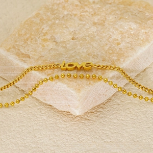 Detail of gold double-layer chain bracelet with love charm on a natural stone background