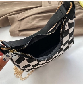 Detail of checkered canvas bag with black leather trim and golden zipper closure
