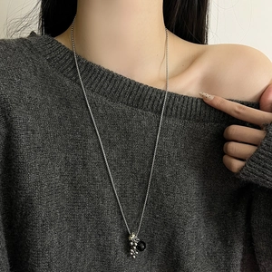 Long collier argenté avec pendentif en perles porté sur un pull en maille gris foncé