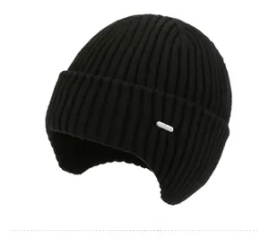 Detail of black rib-knit beanie with ear flaps and oval metal logo plate for winter