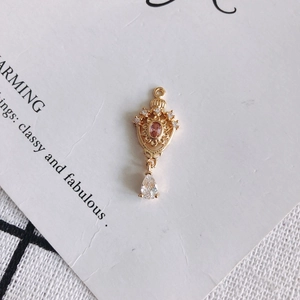 Macro detail of 18K gold crown pendant with pink stone and zircon teardrop on white card