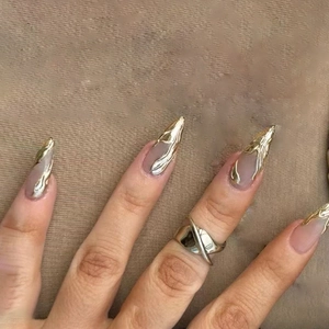 Detail of 3D gold fluid wave stiletto press-on nails with matching gold cross ring accessory