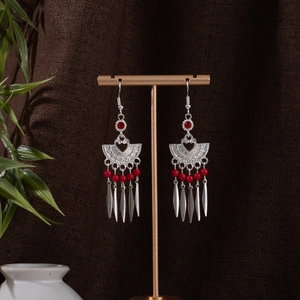 Detail of silver bohemian tassel earrings with red beads on a golden display stand
