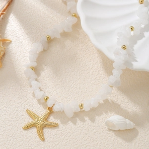 Detail of beaded anklet with white crushed stones and gold starfish charm on beach sand