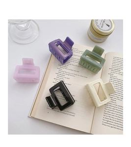 Flat lay of five matte square hair claws in purple, green, beige and black on book pages