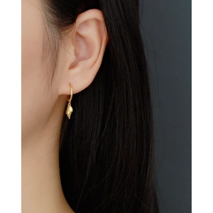 Close-up of a gold s925 shell drop earring worn by a model on a dark background