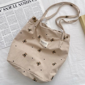 Detailed top view of a beige corduroy tote bag with bear print and lifestyle props