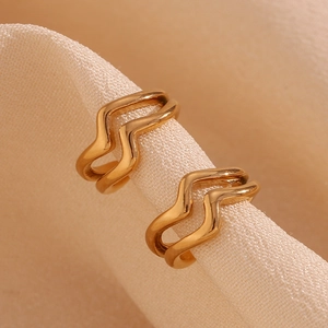 Macro shot of gold double-layer wavy ear cuffs on a textured cream fabric background