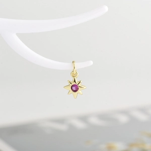 Detailed close-up of a golden star pendant with a centered pink zircon on a white stand