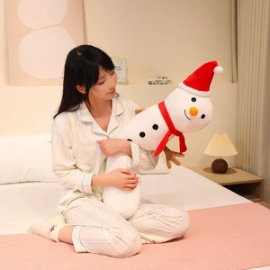 Long plush snowman body pillow with red Christmas hat held by a model on bed