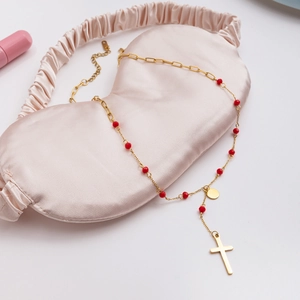 Detailed view of 18K gold stainless steel cross necklace with red beads on pink silk