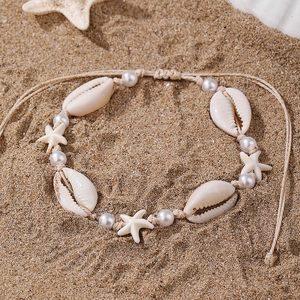Adjustable beige anklet with white shells, starfish and pearls on a beach sand background