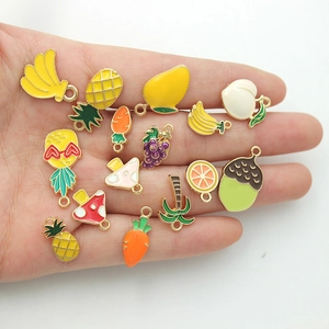 Assorted colorful enamel fruit and vegetable alloy pendants displayed on a palm