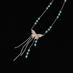 Detailed macro shot of silver butterfly pendant with blue beads and flowing tassels