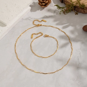 Detailed close-up of 18K gold stainless steel necklace and bracelet on marble surface