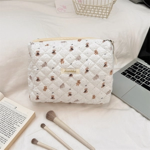 Quilted makeup bag with bear prints on a white bed with laptop and beauty tools