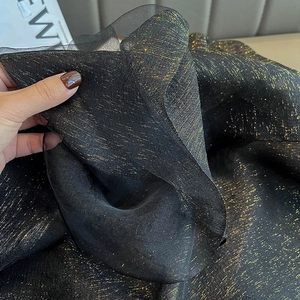 Detailed close-up of premium black silk chiffon fabric with shimmering gold metallic threads