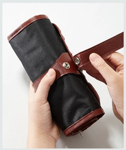 Close-up of black canvas tool roll bag with brown leather strap and metal buckle fastener