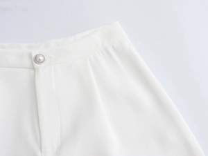 Detail of white trousers featuring an elegant pearl button and tailored waistline
