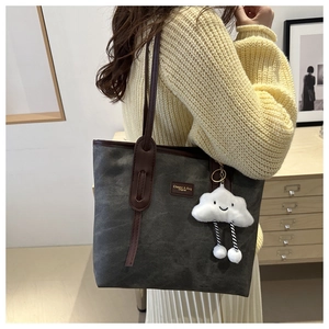 Detail of grey canvas tote bag with brown leather straps and a plush cloud charm