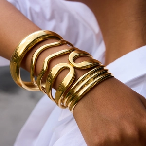 Detail of 18K gold-plated double layered wave bangles worn on wrist over a white shirt