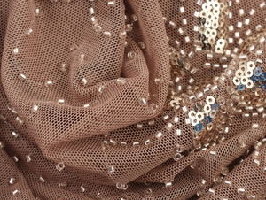 Detailed macro view of beige mesh fabric with intricate beadwork and shimmering sequins