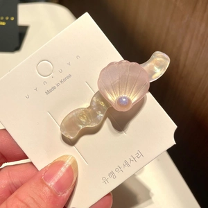 Close-up of pink shell-shaped hair clip with iridescent resin texture and pearl accent