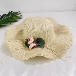 Détail du chapeau de paille beige à bord ondulé avec roses roses en soie et feuilles décoratives