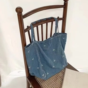 Close-up of blue denim tote bag with white bow embroidery hanging on a vintage wooden chair
