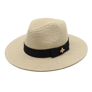 Detail of straw fedora hat with black grosgrain ribbon and golden bee metal ornament