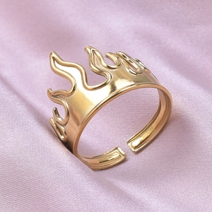 Detail shot of golden flame-shaped open ring on a pink silk fabric background