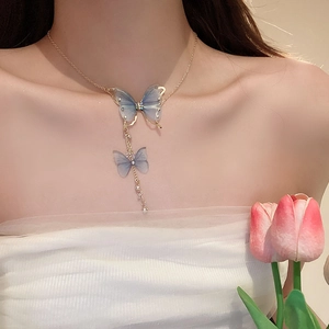 Detail of gold butterfly necklace with blue wings, shimmering rhinestones and a pearl drop