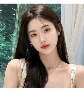 Model wearing blue butterfly enamel earrings and a pearl necklace by a sunlit window