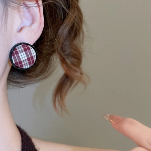 Detail of a red and white checkered fabric stud earring with black trim on a model ear
