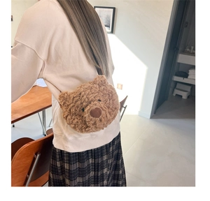 Brown plush teddy bear head crossbody bag worn by model in a cozy indoor setting