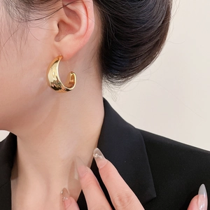 Side view of a gold wide C-shaped earring featuring a smooth polished metallic texture