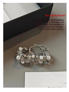 Detail of silver hollow floral hoop earrings with pearls and rhinestones on a surface