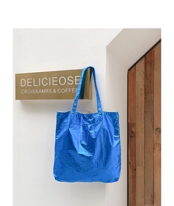 Detail of blue metallic nylon tote bag hanging on a wooden door in minimalist setting