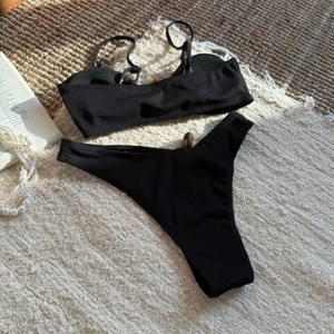 Flat lay of black ribbed bikini set on woven rug with lifestyle accessories
