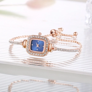 Detail shot of a rose gold square watch with blue dial and crystals on textured surface