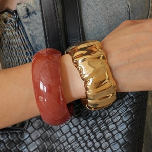 Close-up of a resin bangle paired with a golden ripple textured wide metal bracelet