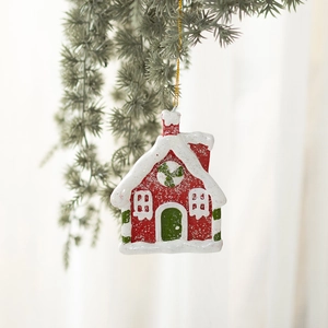 Christmas red gingerbread house ornament with snow details hanging on a pine branch