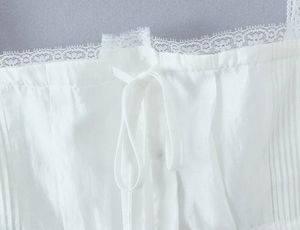 Close-up of white pleated fabric with delicate eyelash lace trim and center ribbon bow