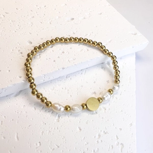 Detail of beaded gold bracelet with baroque pearls and round flat charm on stone