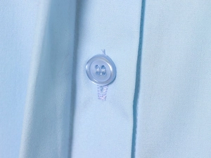 Detailed macro view of light blue shirt fabric texture with matching four-hole button