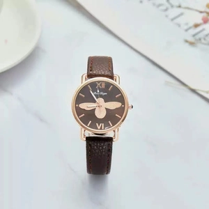 Detail of rose gold watch face with brown leather strap and bee pattern dial