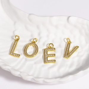 Detail of gold LOVE letter pendants with inlaid cubic zirconia on white ceramic tray