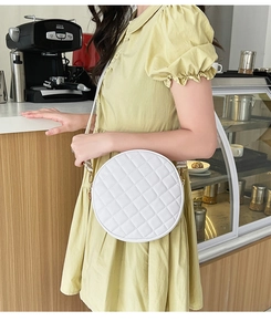 Close-up of a white quilted round crossbody bag worn by a model in a modern cafe setting